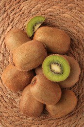 Photo of Heap of whole and cut fresh kiwis on wicker mat, flat lay