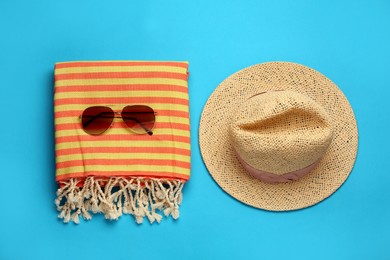 Photo of Beach towel, straw hat and sunglasses on light blue background, flat lay