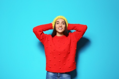 Young woman in warm sweater and hat on color background. Celebrating Christmas