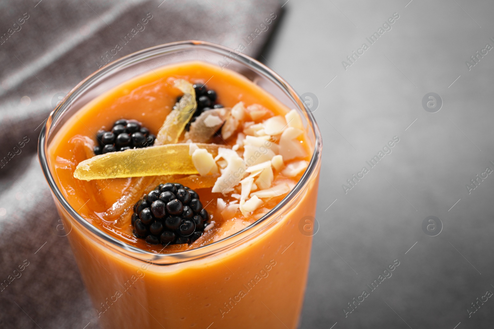 Photo of Glass of delicious smoothie with blackberries, candied mango and almond on grey table, closeup. Space for text