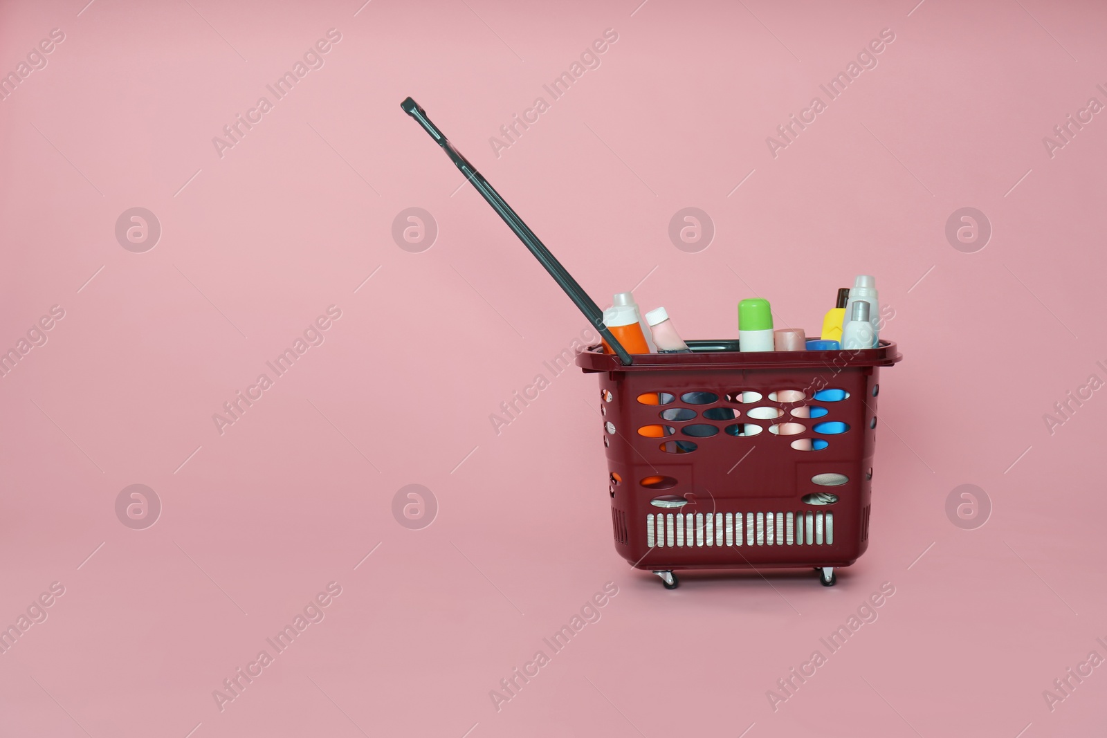 Photo of Shopping basket full of cleaning supplies on pink background. Space for text