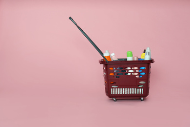 Shopping basket full of cleaning supplies on pink background. Space for text