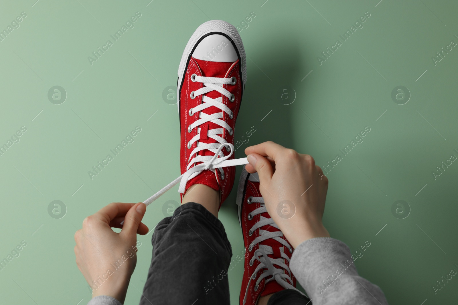 Photo of Woman tying laces of gumshoes on pale green background, closeup