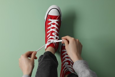 Woman tying laces of gumshoes on pale green background, closeup