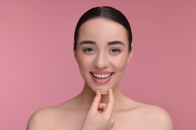 Photo of Beautiful young woman with vitamin pill on pink background