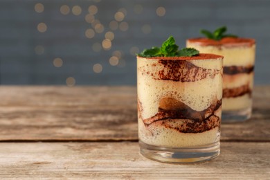 Photo of Tasty tiramisu and mint in glasses on wooden table, closeup. Space for text