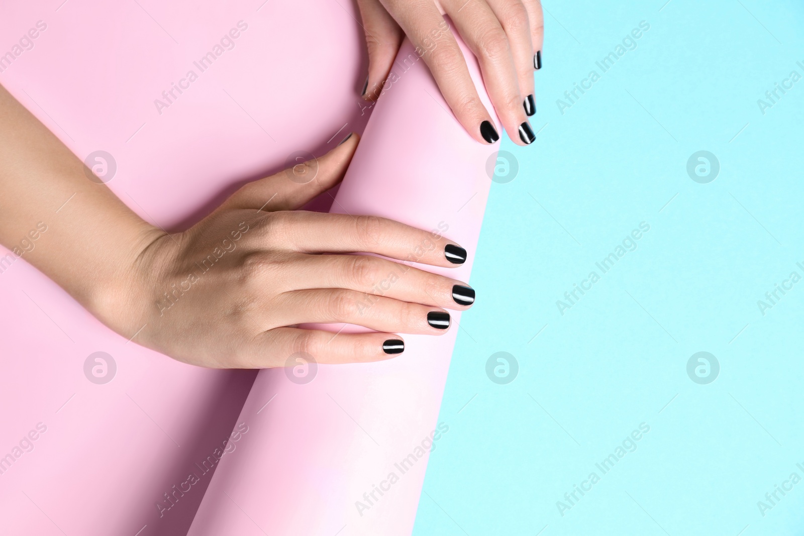 Photo of Woman with black manicure holding paper roll on color background, space for text. Nail polish trends