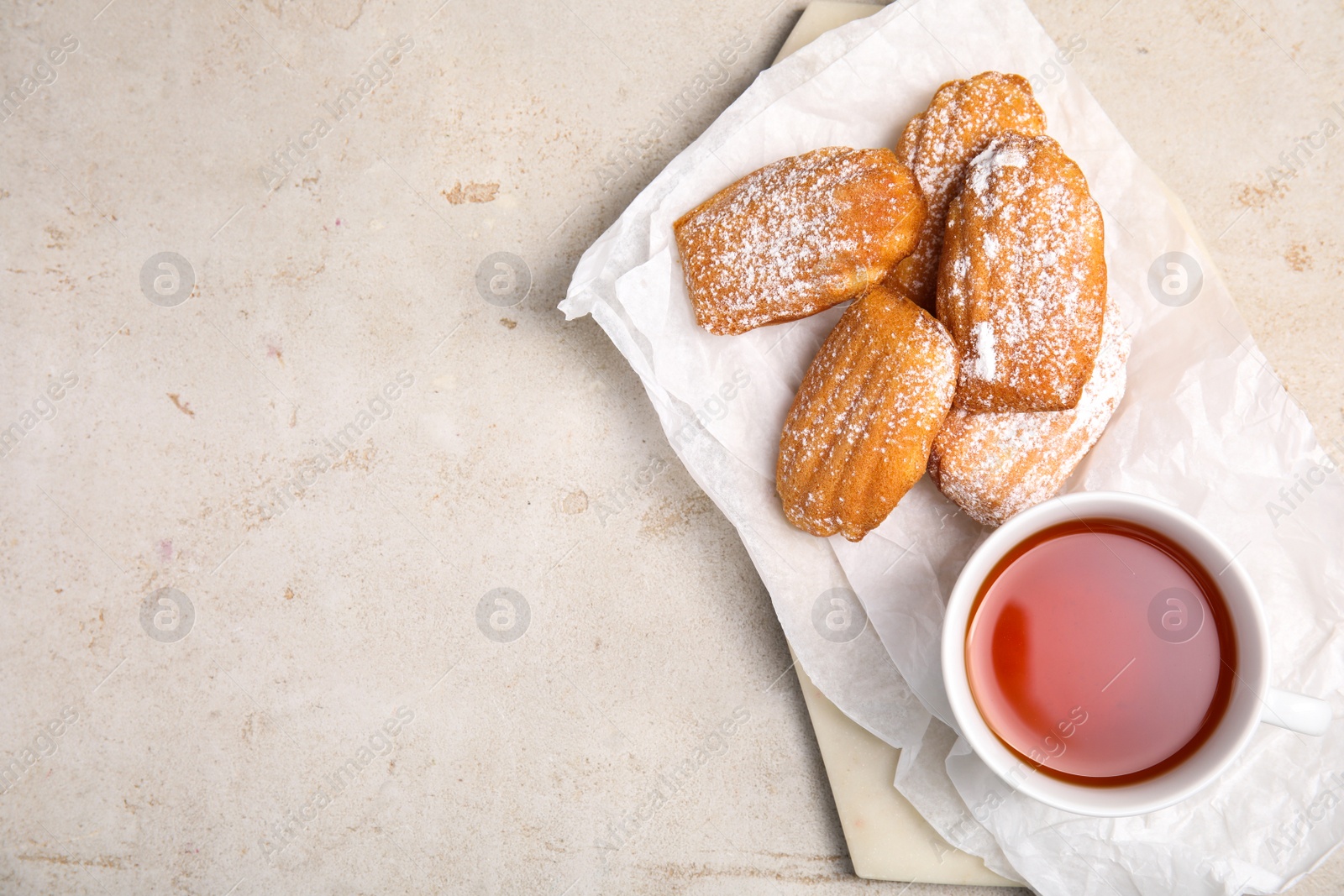 Photo of Delicious madeleine cakes with powdered sugar and tea on light grey table, top view. Space for text