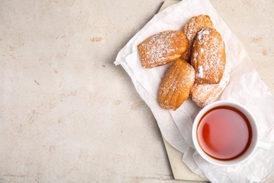 Delicious madeleine cakes with powdered sugar and tea on light grey table, top view. Space for text