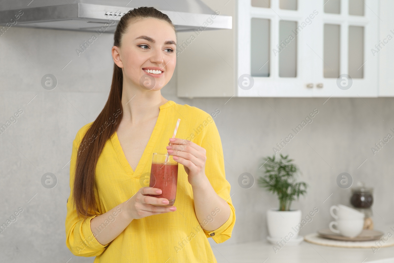 Photo of Beautiful young woman with delicious smoothie in kitchen. Space for text