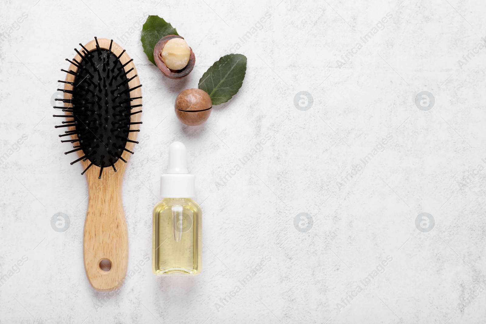 Photo of Delicious organic Macadamia nuts, natural oil, brush and green leaves on white textured table, flat lay. Space for text