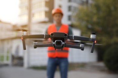 Builder operating drone with remote control at construction site, focus on quadcopter. Aerial survey