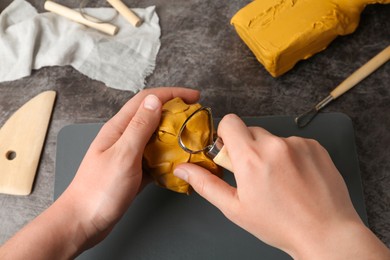 Photo of Woman working with loop tool and clay at grey stone table, closeup