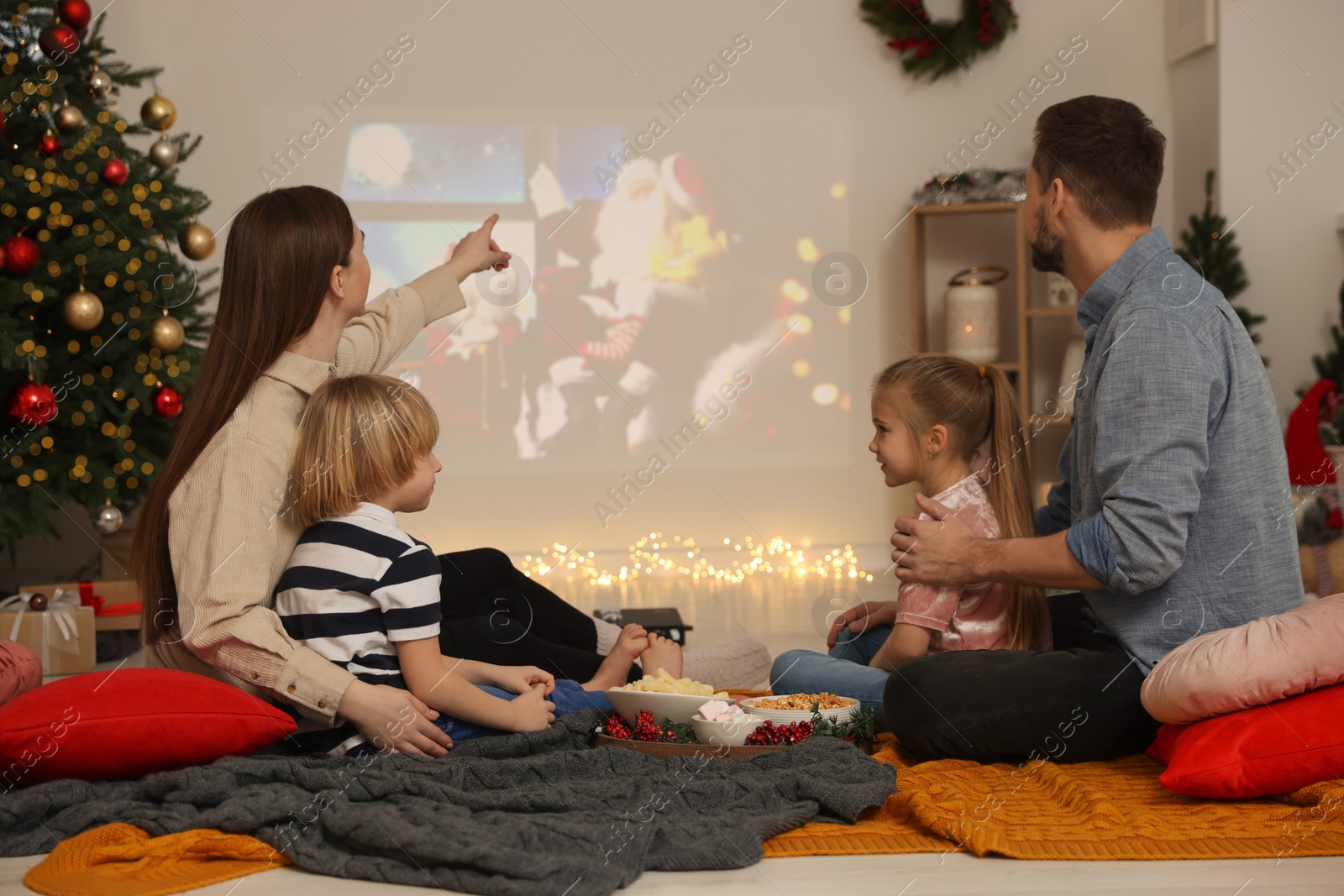 Photo of Family watching Christmas movie via video projector in cosy room. Winter holidays atmosphere