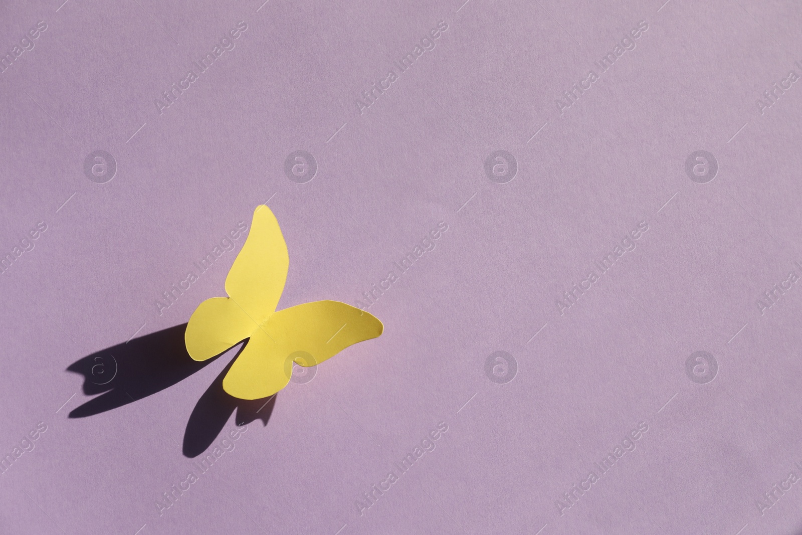 Photo of Yellow paper butterfly on violet background, top view. Space for text