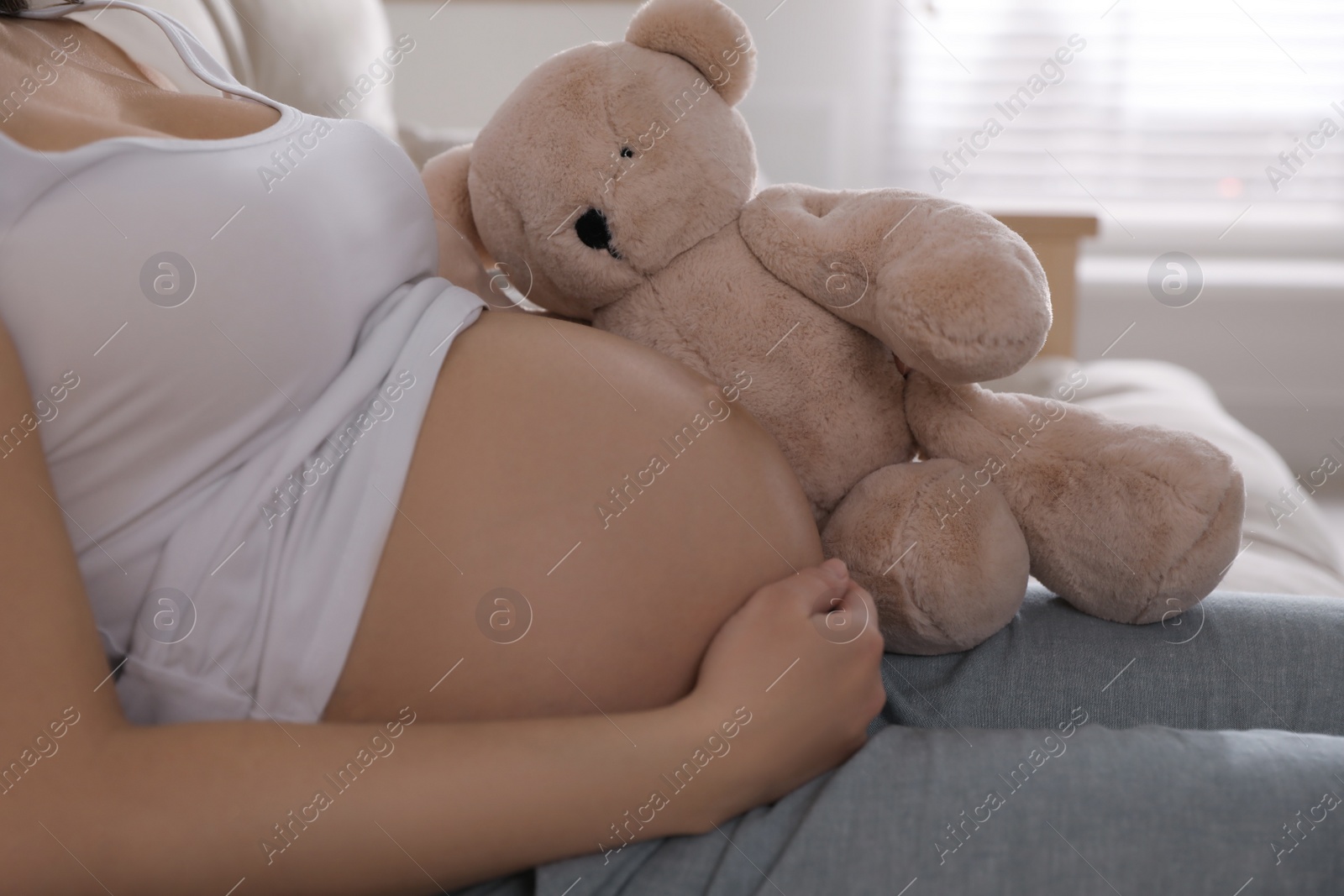 Photo of Young pregnant woman with toy bear at home, closeup