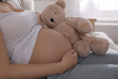 Young pregnant woman with toy bear at home, closeup