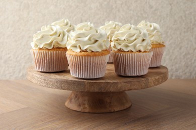 Photo of Tasty vanilla cupcakes with cream on wooden table