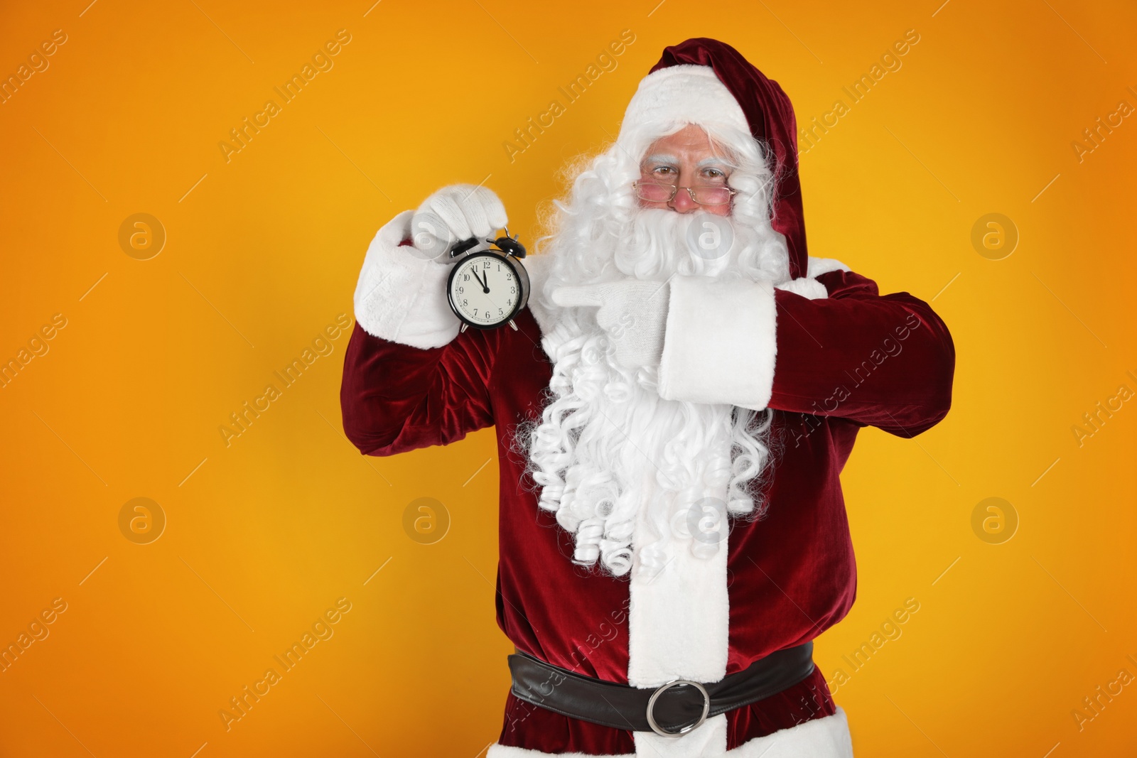 Photo of Santa Claus holding alarm clock on yellow background. Christmas countdown