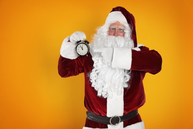 Santa Claus holding alarm clock on yellow background. Christmas countdown