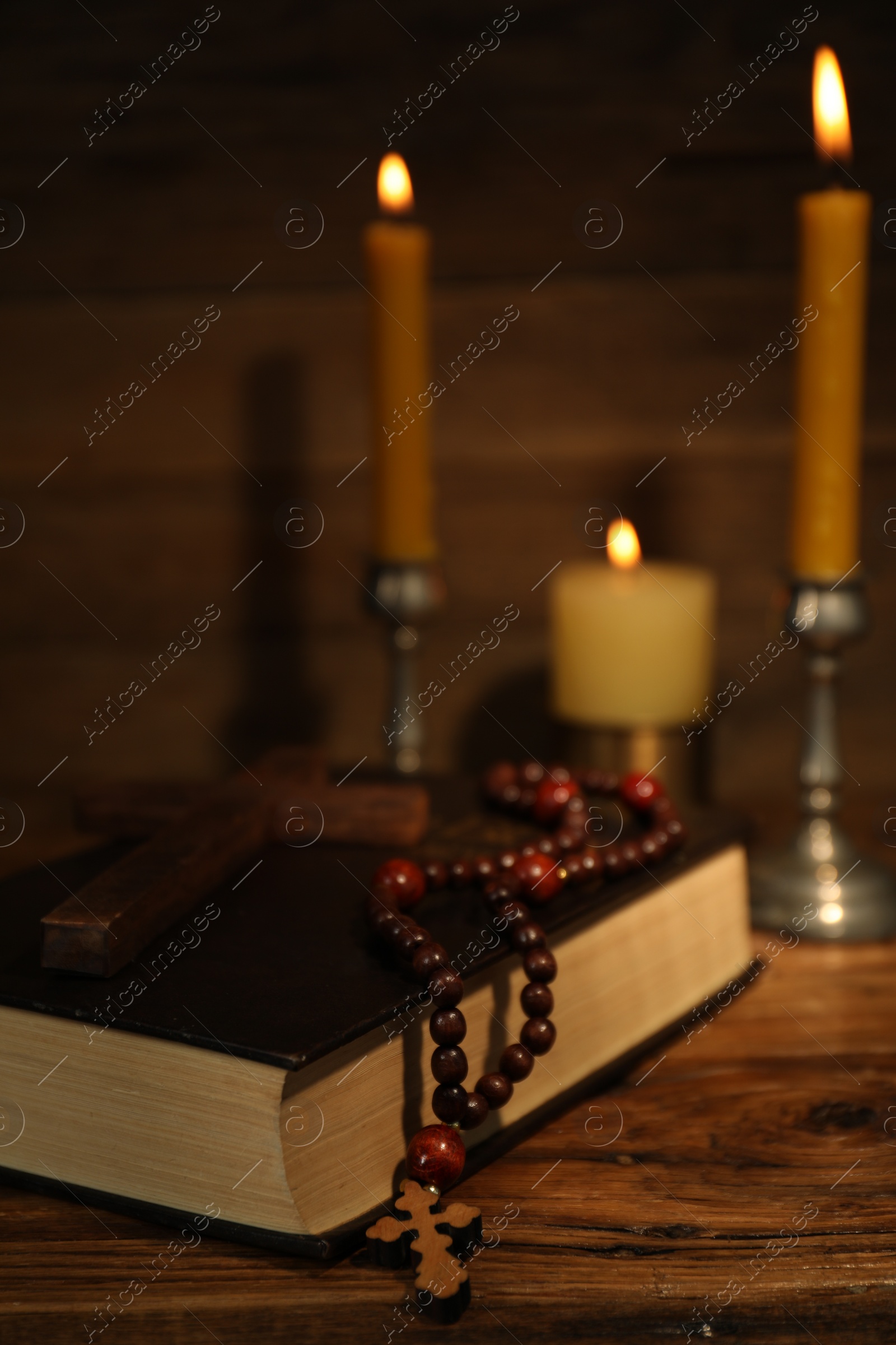 Photo of Church candles, cross, Bible and rosary beads on wooden table