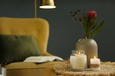 Vase with beautiful protea flowers and burning candles on wooden table indoors, space for text. Interior elements