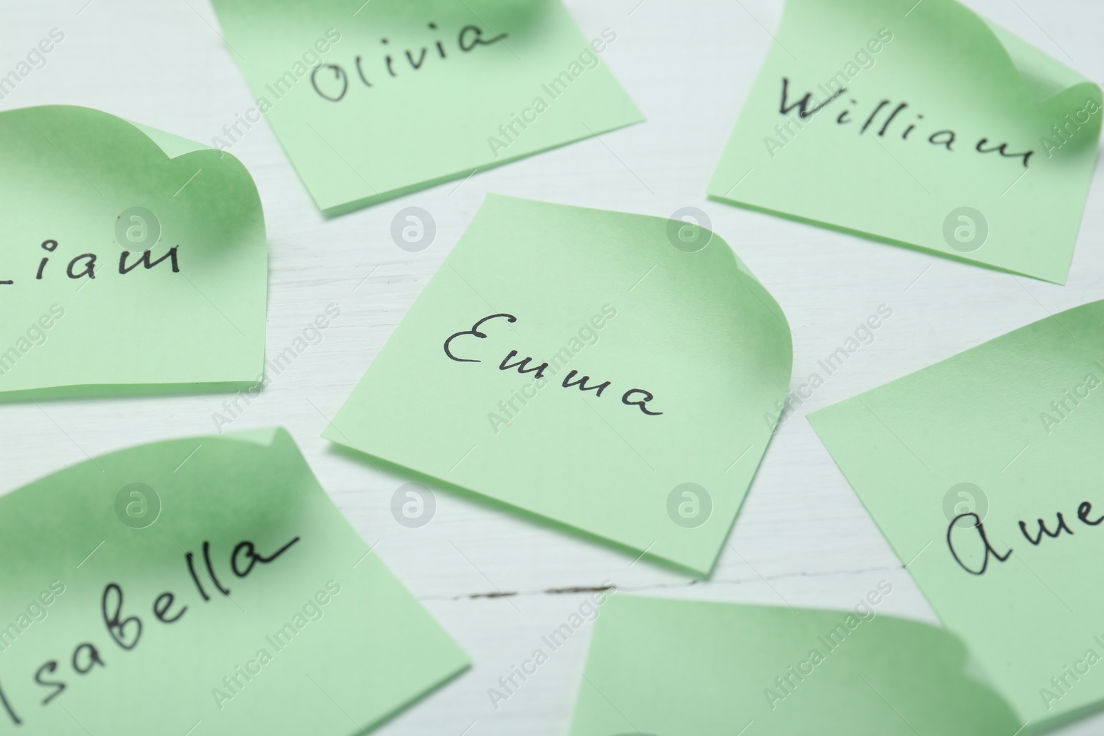 Photo of Paper stickers with different names on white wooden table, closeup. Choosing baby's name