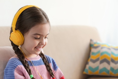Photo of Cute child with headphones on sofa indoors. Space for text