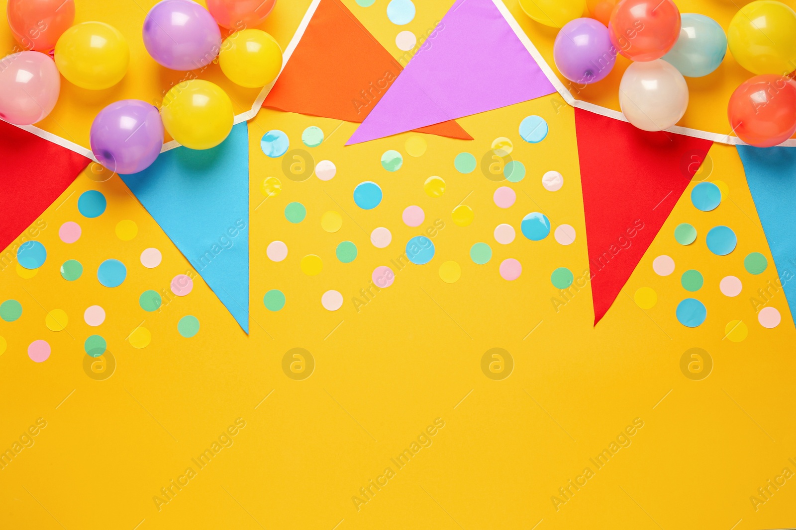 Photo of Bunting with colorful triangular flags and other festive decor on yellow background, flat lay. Space for text