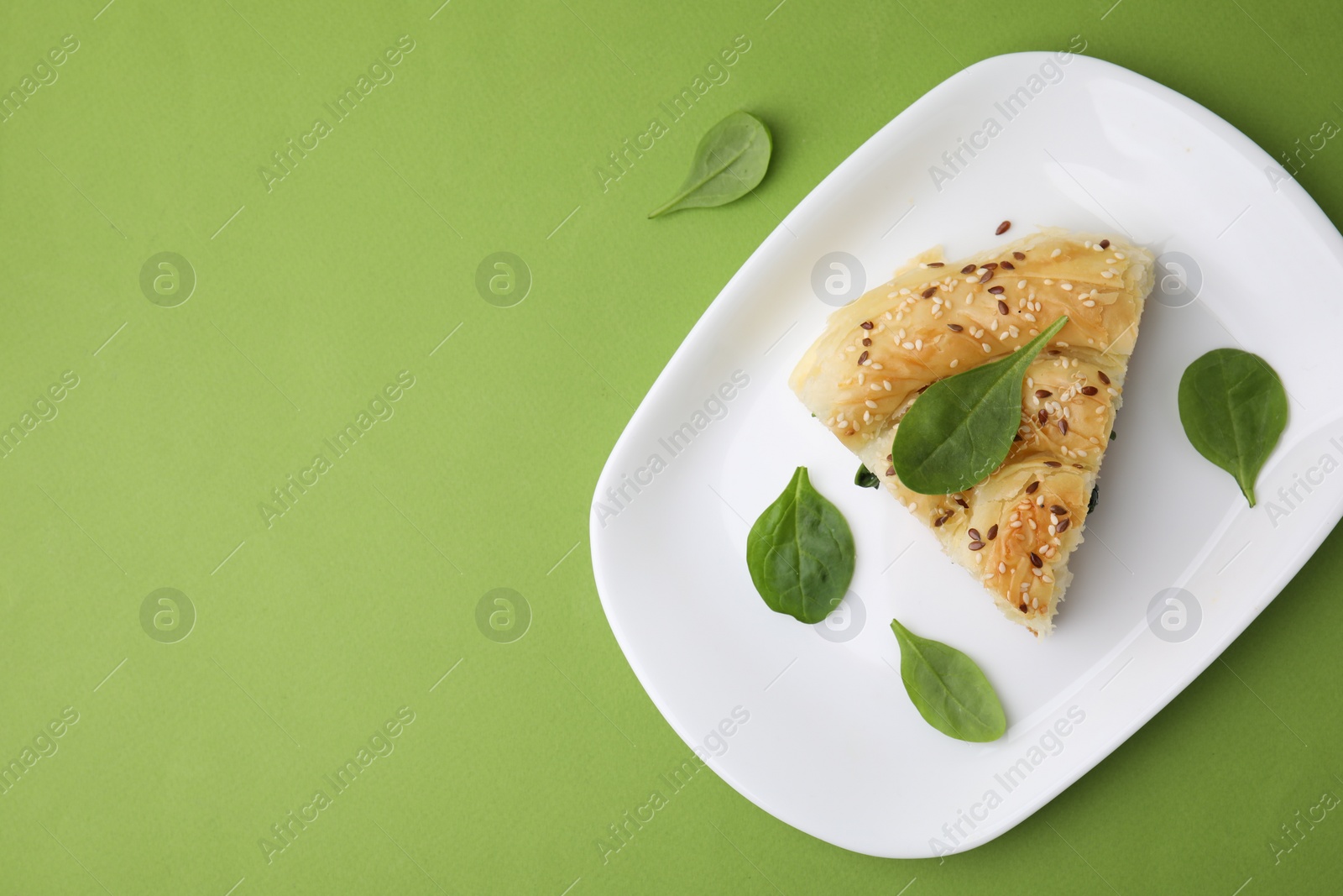 Photo of Piece of delicious puff pastry with spinach on green background, top view. Space for text