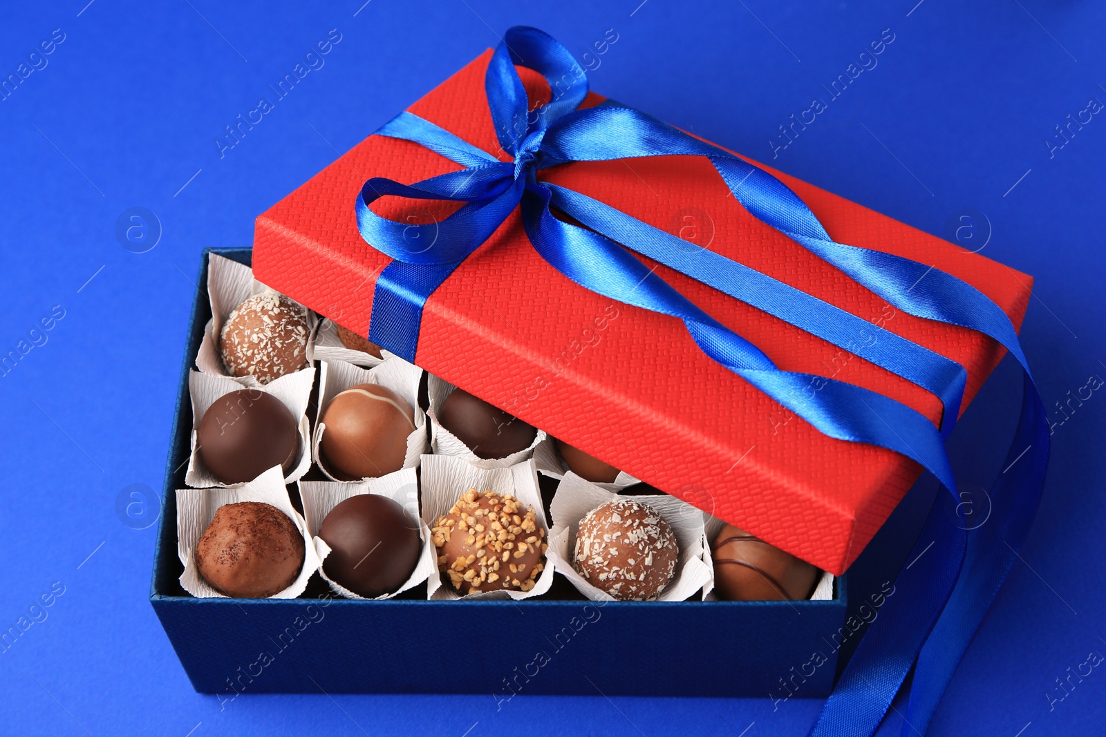 Photo of Box with delicious chocolate candies on blue background, closeup