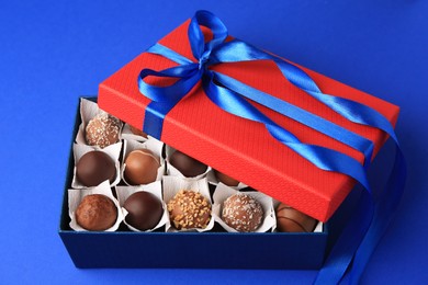 Photo of Box with delicious chocolate candies on blue background, closeup