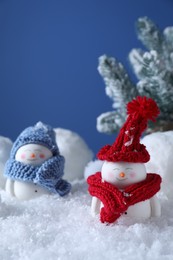 Photo of Cute decorative snowmen and fir tree on snow against blue background