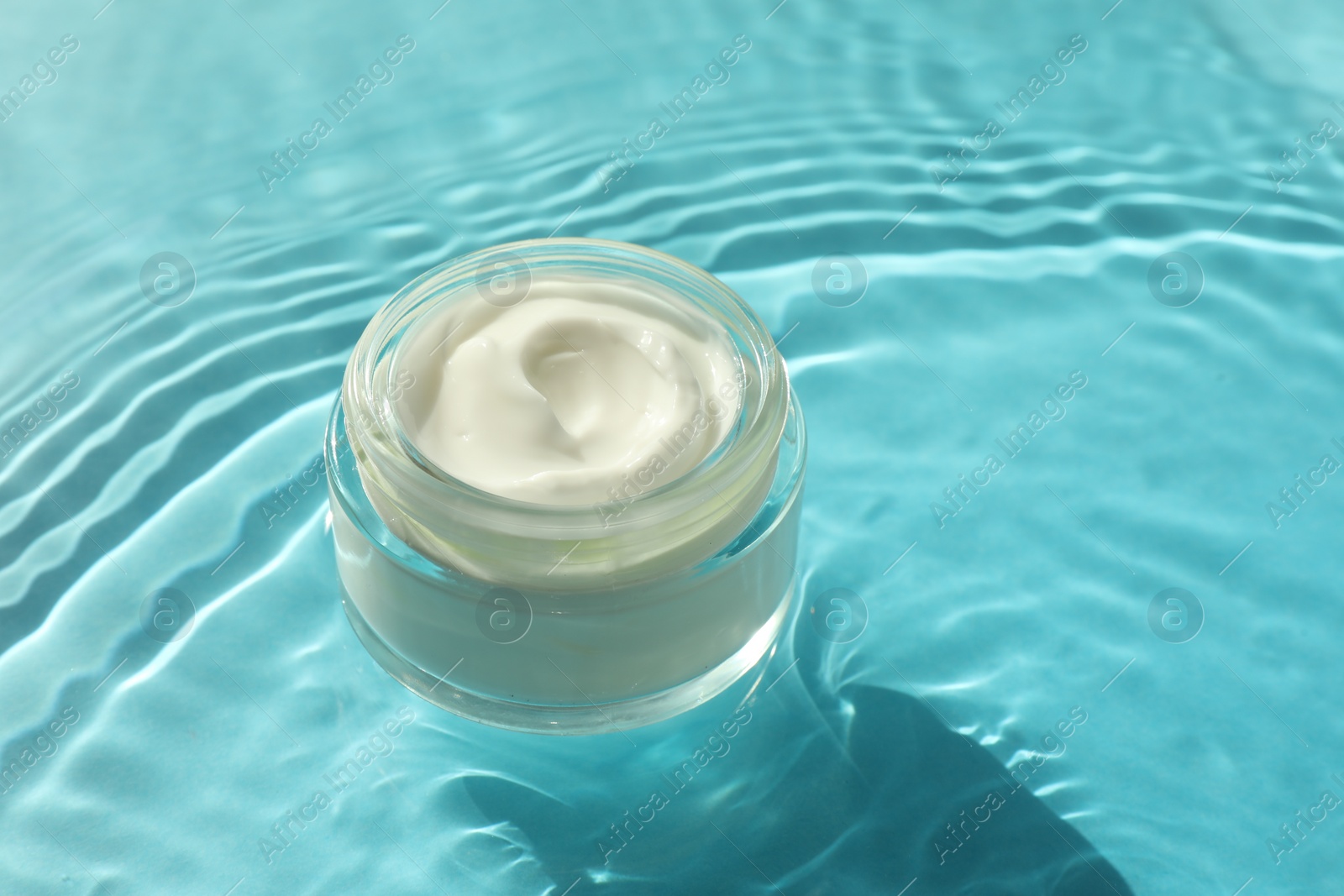 Photo of Jar with moisturizing cream in water on light blue background