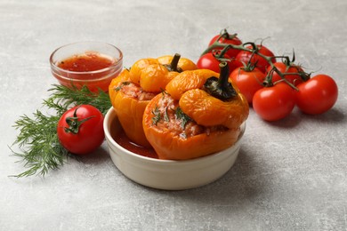 Photo of Tasty stuffed peppers in bowl, dill, tomatoes and sauce on light grey table