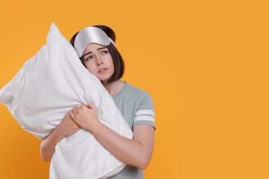 Photo of Unhappy young woman with sleep mask and pillow on yellow background, space for text. Insomnia problem