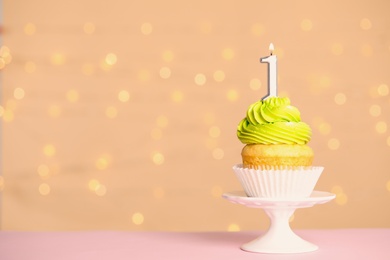Photo of Birthday cupcake with number one candle on stand against festive lights, space for text