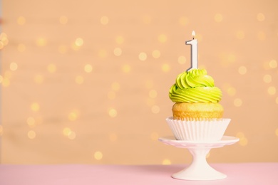 Birthday cupcake with number one candle on stand against festive lights, space for text