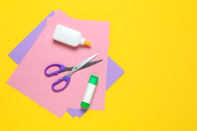 Photo of Glue, colorful paper and scissors on yellow background, flat lay. Space for text