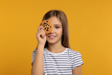 Cute girl with chocolate chip cookie on orange background