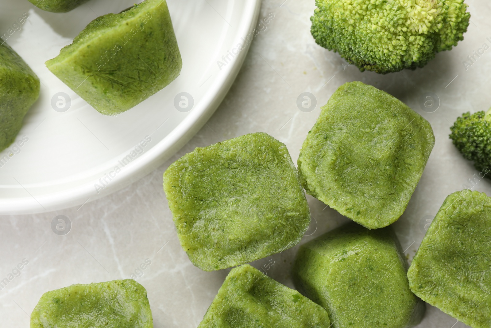 Photo of Frozen broccoli puree cubes with ingredient on marble table, flat lay