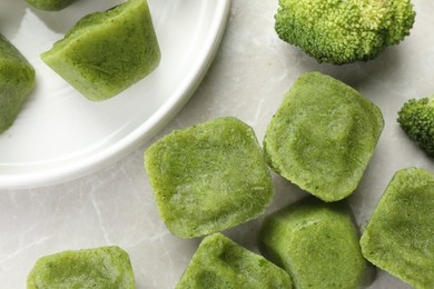 Frozen broccoli puree cubes with ingredient on marble table, flat lay