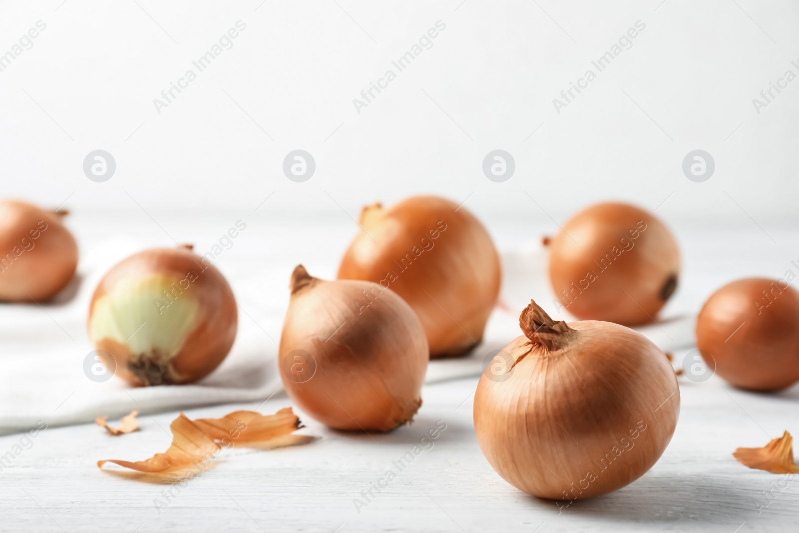 Photo of Ripe yellow onion bulbs on white wooden table