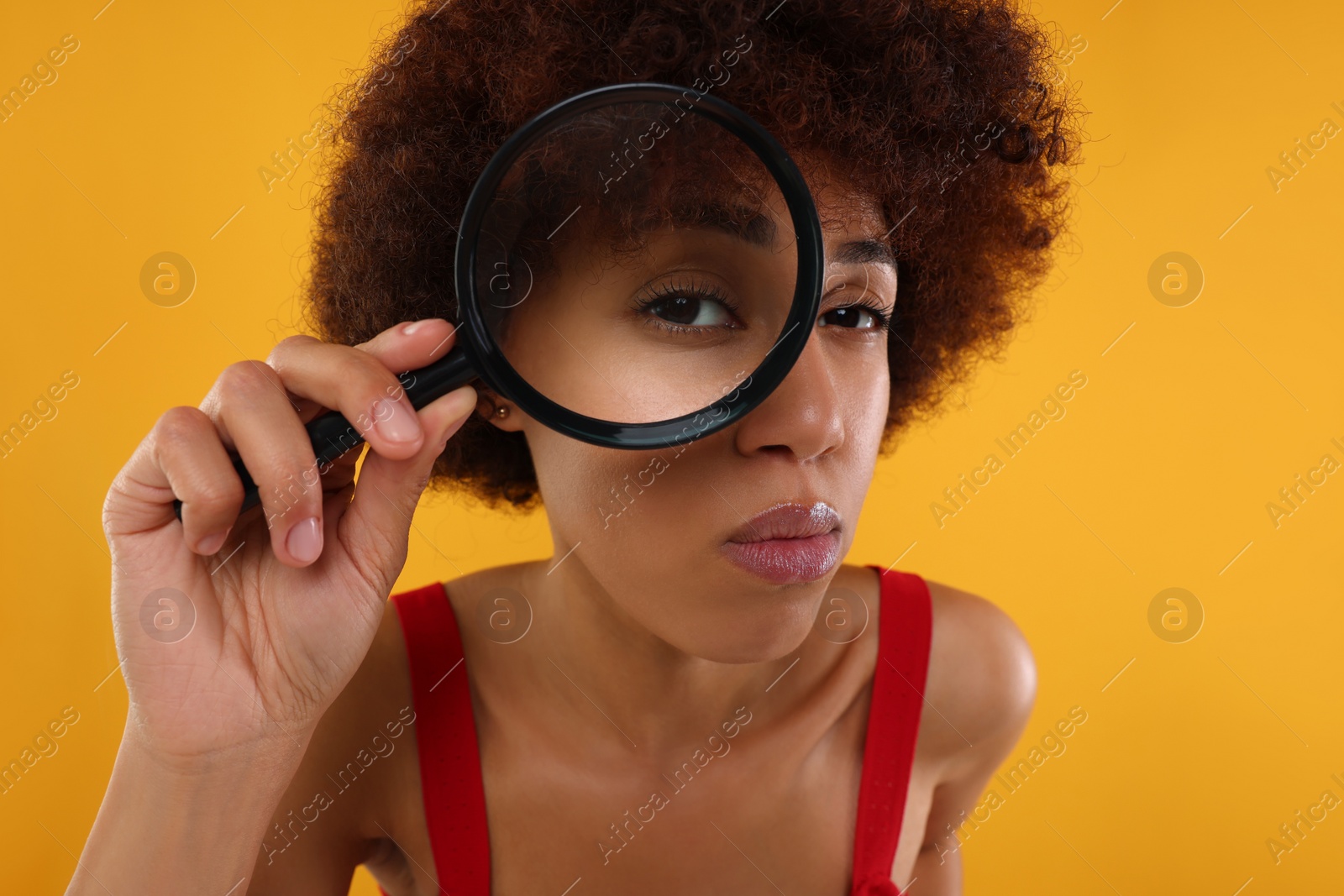 Photo of Young woman looking through magnifier glass on orange background