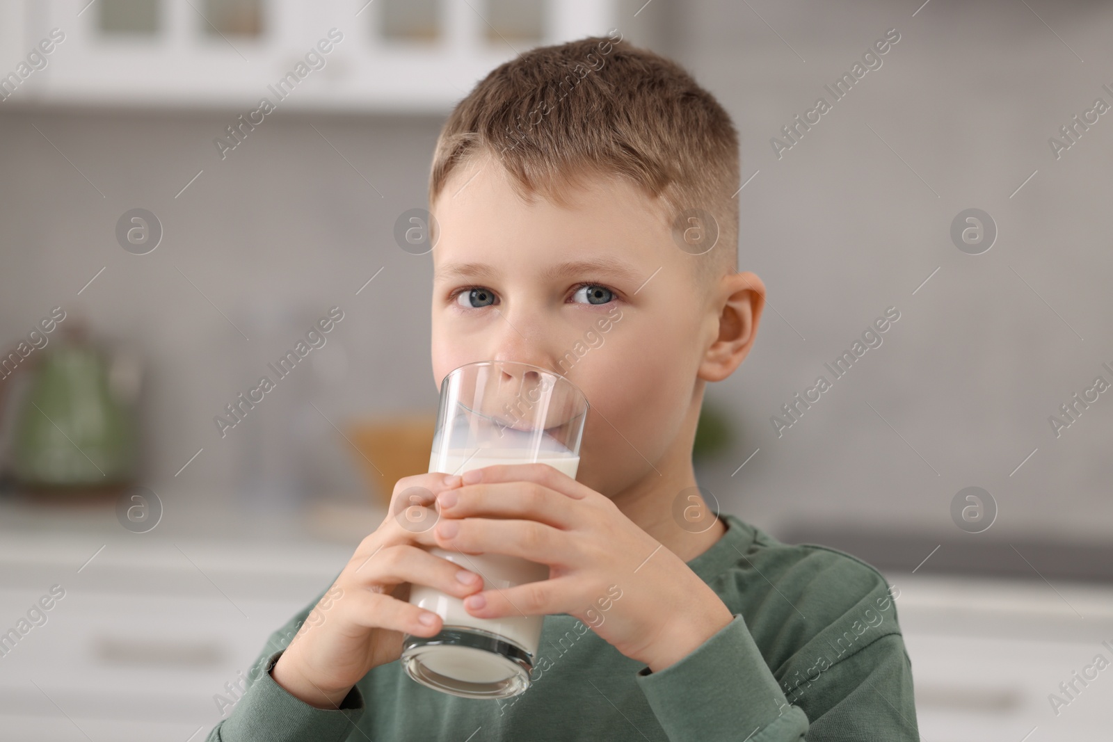 Photo of Cute boy drinking fresh milk from glass indoors