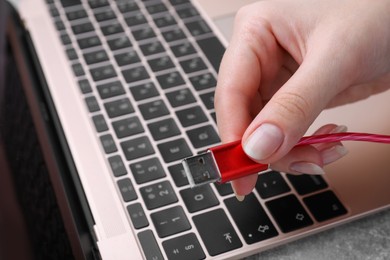 Photo of Woman holding USB cable near laptop at grey table, closeup