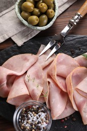 Photo of Tasty ham, olives, sea salt, peppercorns and carving fork on table, flat lay