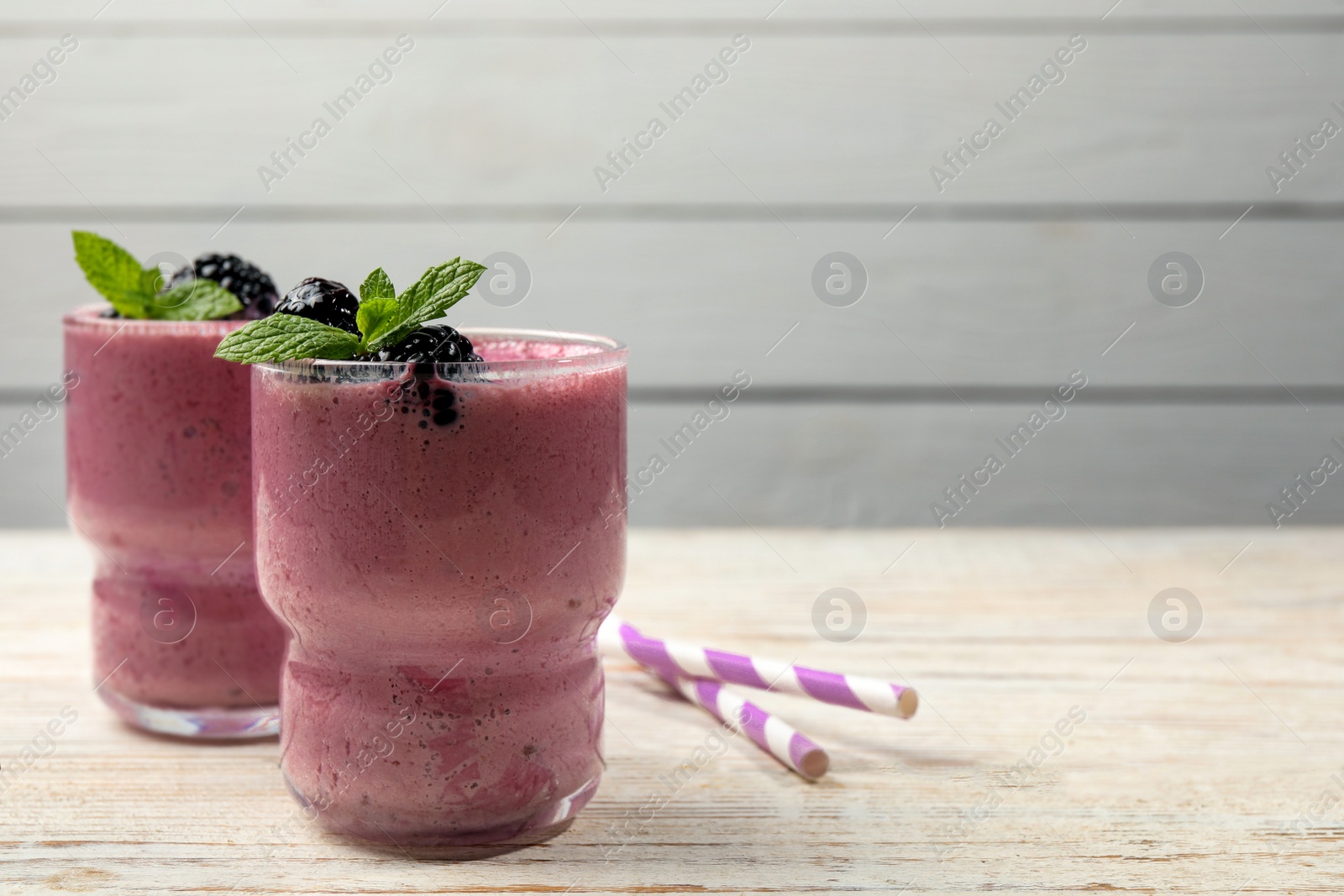 Photo of Glasses of blackberry smoothie with mint and berries on light wooden table,. Space for text