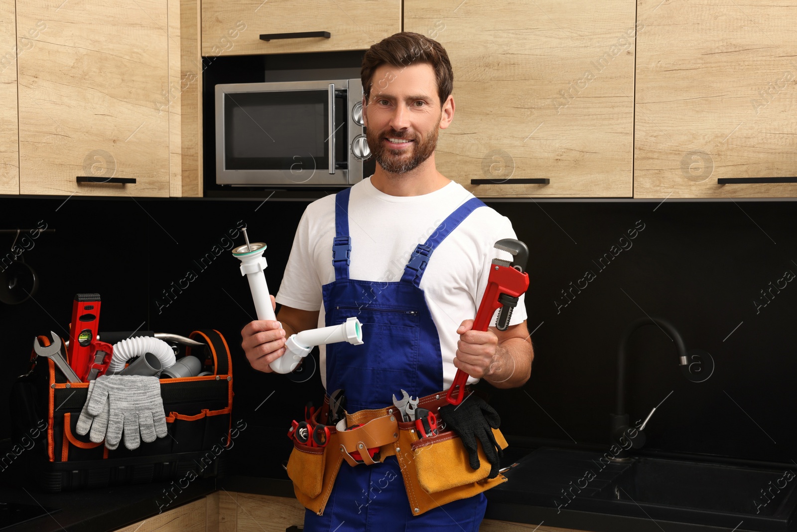 Photo of Professional plumber with corrugated pipe and wrench in kitchen