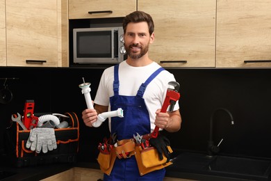Professional plumber with corrugated pipe and wrench in kitchen